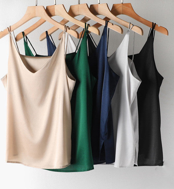 Set of five satin camisoles in beige, green, navy, white, and black on hangers against a gray background.