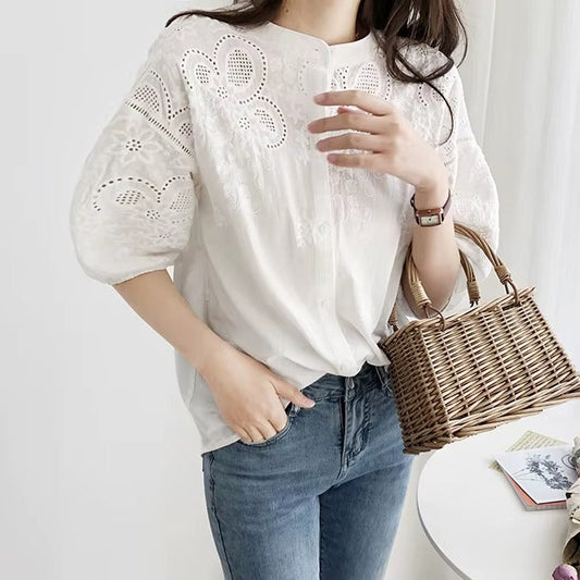 Person wearing a white blouse with lace details and blue jeans, holding a woven handbag.