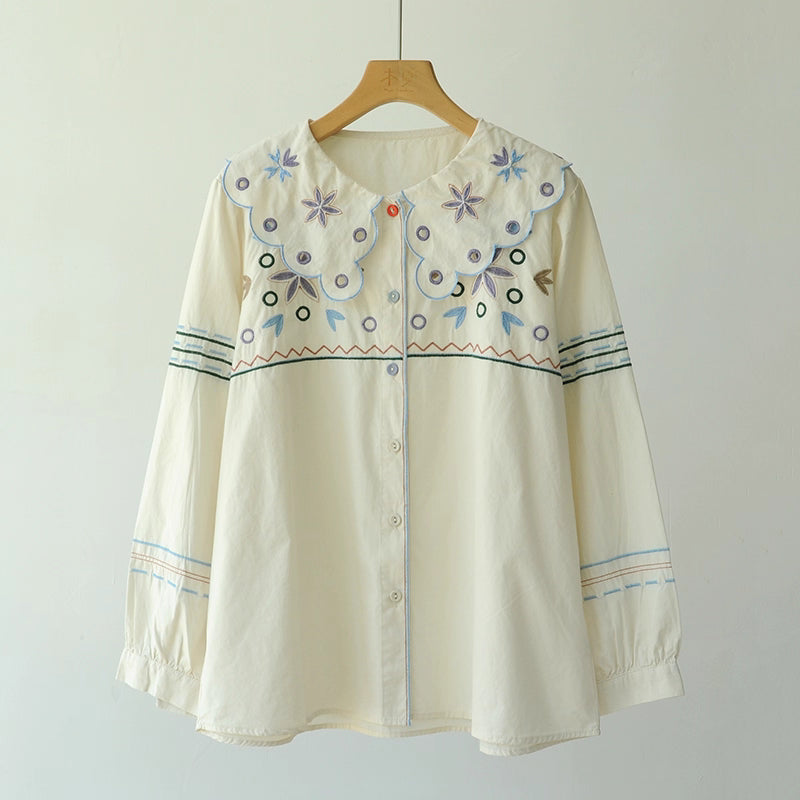 Embroidered blouse on a wooden hanger against a plain background
