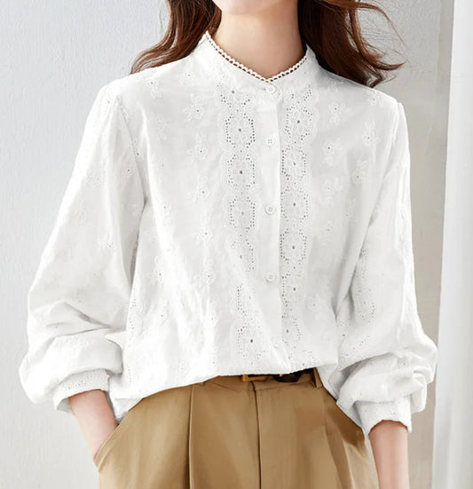 Woman wearing a white blouse with lace details and beige pants against a plain background