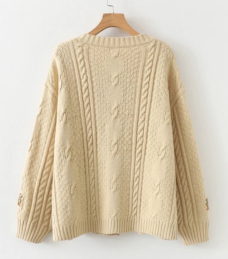Beige cable knit sweater on a wooden hanger against a white background