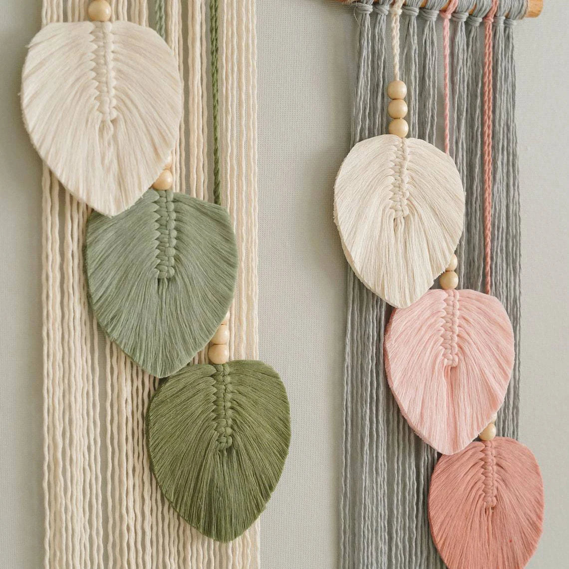 Decorative wall hanging with leaf-shaped macramé elements in pastel colors on a neutral background.