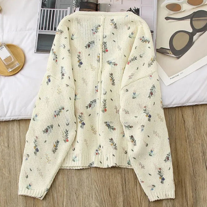 Floral-patterned cardigan on a wooden surface with a magazine and sunglasses in the background.