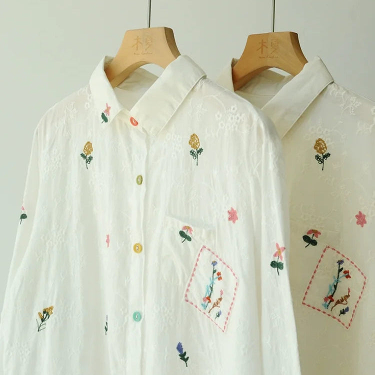 White shirt with floral embroidery on wooden hangers against a white background