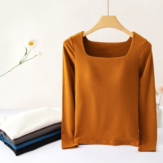 Mustard yellow long-sleeve top on a wooden hanger against a white background