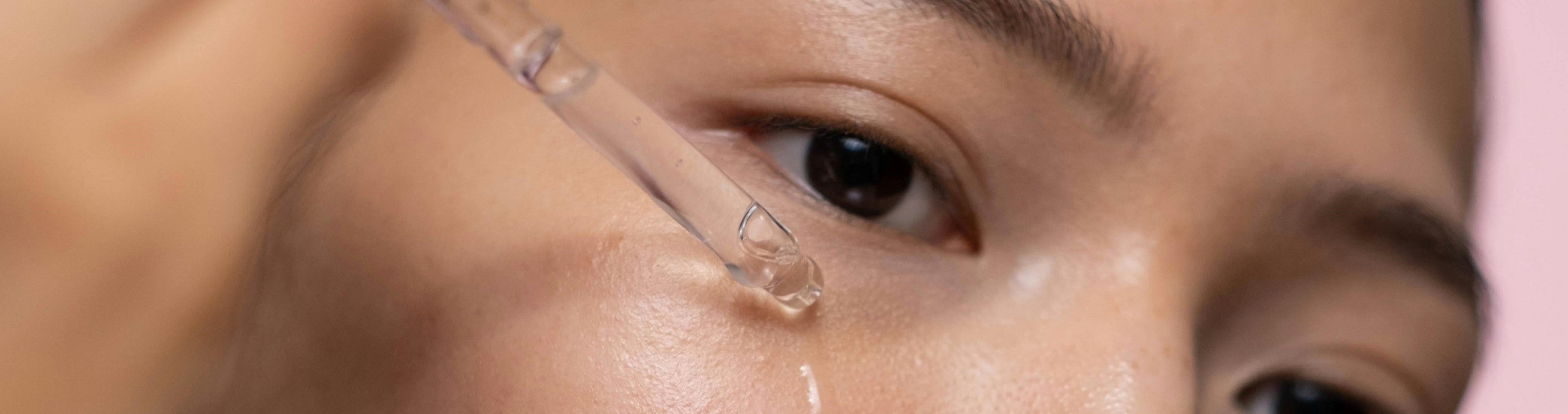Close-up of a person applying a dropper to their eye with a pink background
