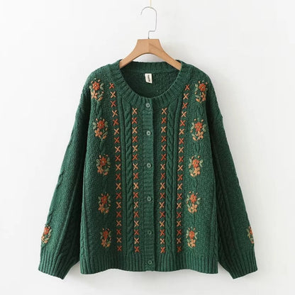 Green sweater with floral patterns on a wooden hanger against a white background