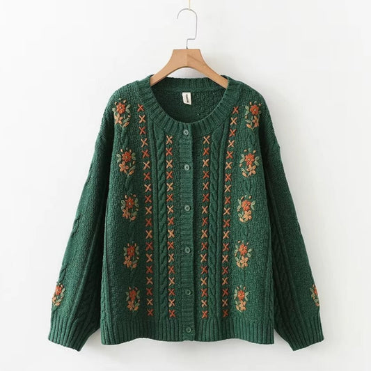 Green sweater with floral patterns on a wooden hanger against a white background