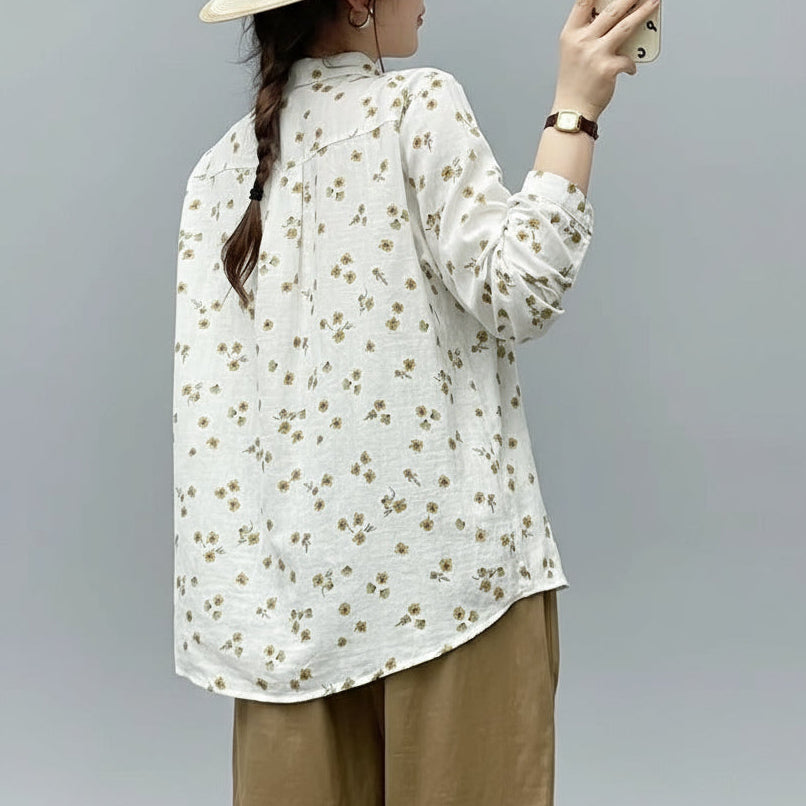Person wearing a floral blouse and wide-brimmed hat, taking a selfie against a plain background