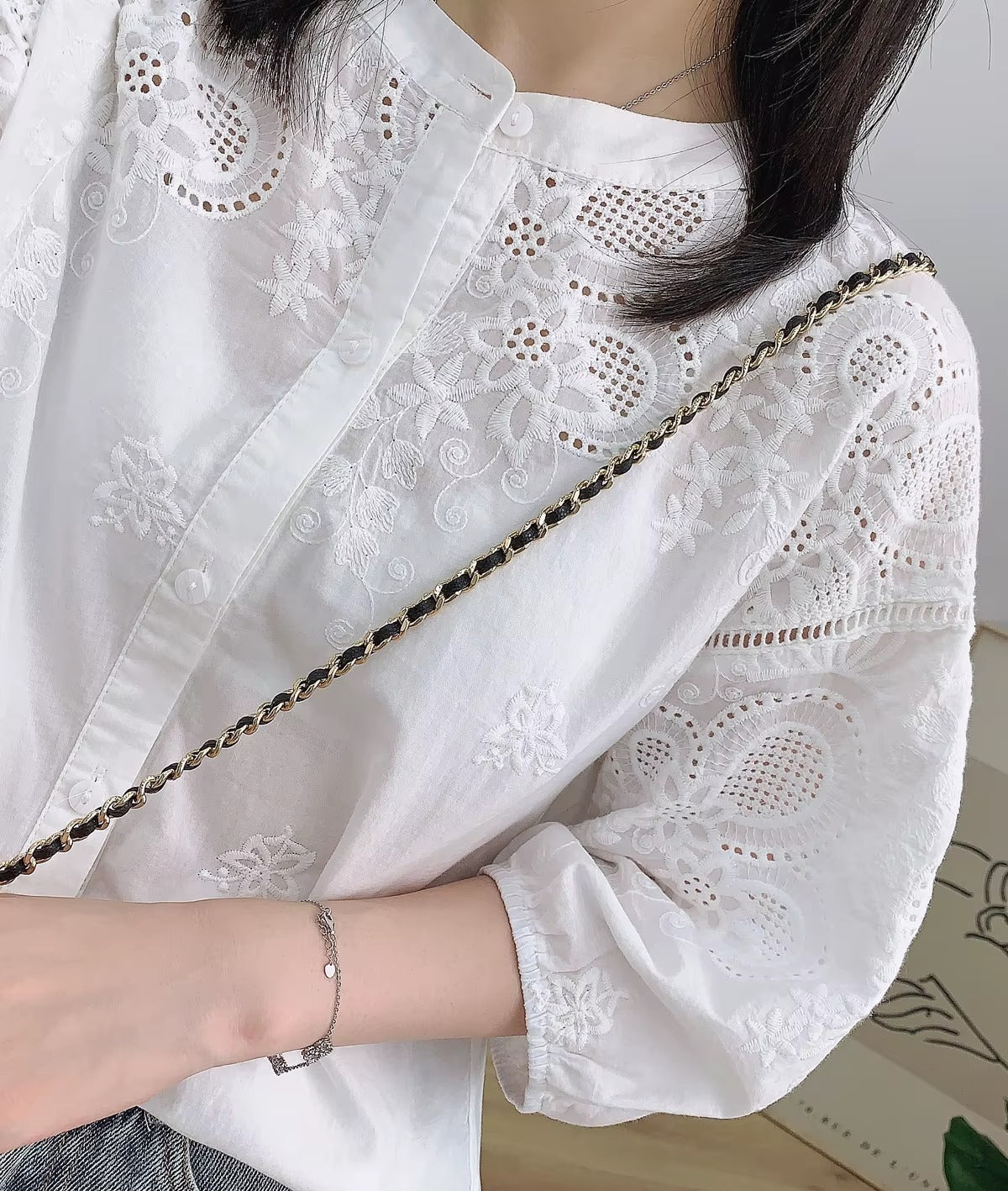 Person wearing a white embroidered blouse with a gold chain strap over a shoulder.