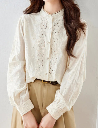 Woman wearing a white lace blouse and beige pants against a plain background