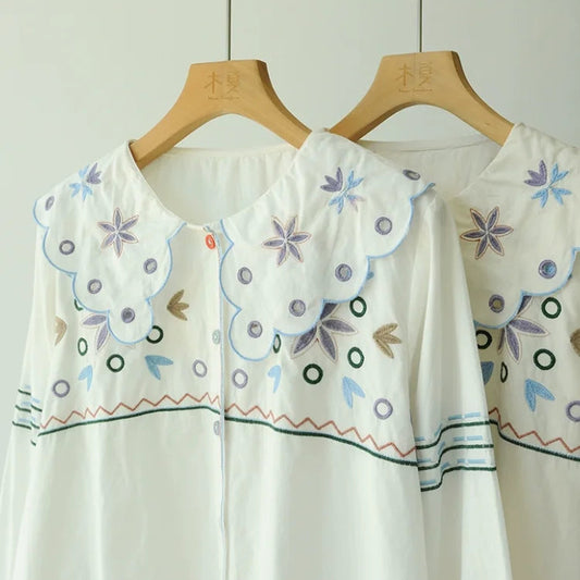White blouse with floral embroidery on a wooden hanger against a white background