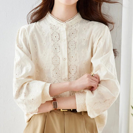 Person wearing a white lace blouse and beige pants against a plain background