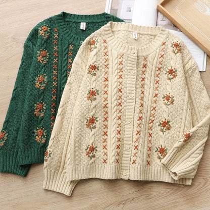 Two sweaters, one green and one beige, with floral patterns on a wooden surface.