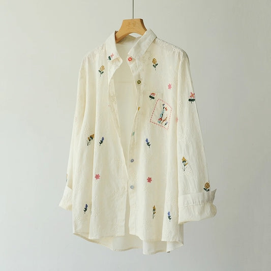 Beige shirt with floral embroidery on a wooden hanger against a plain background