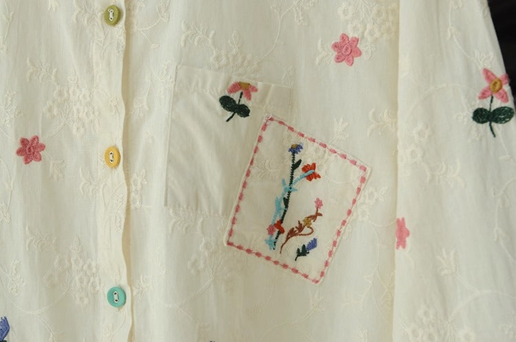 White blouse with floral embroidery and buttons on a plain background