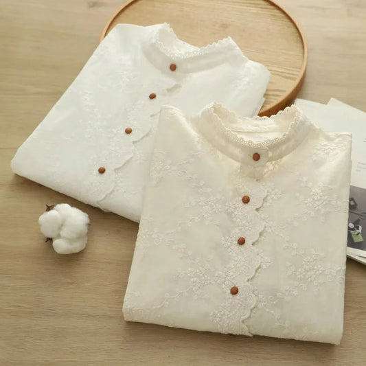 Two white shirts with lace details and brown buttons on a wooden surface.